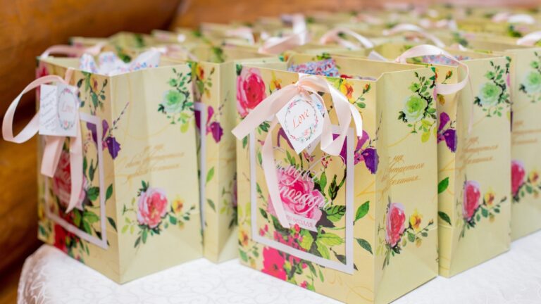 Floral welcome bags with ribbon tags sit on a reception table