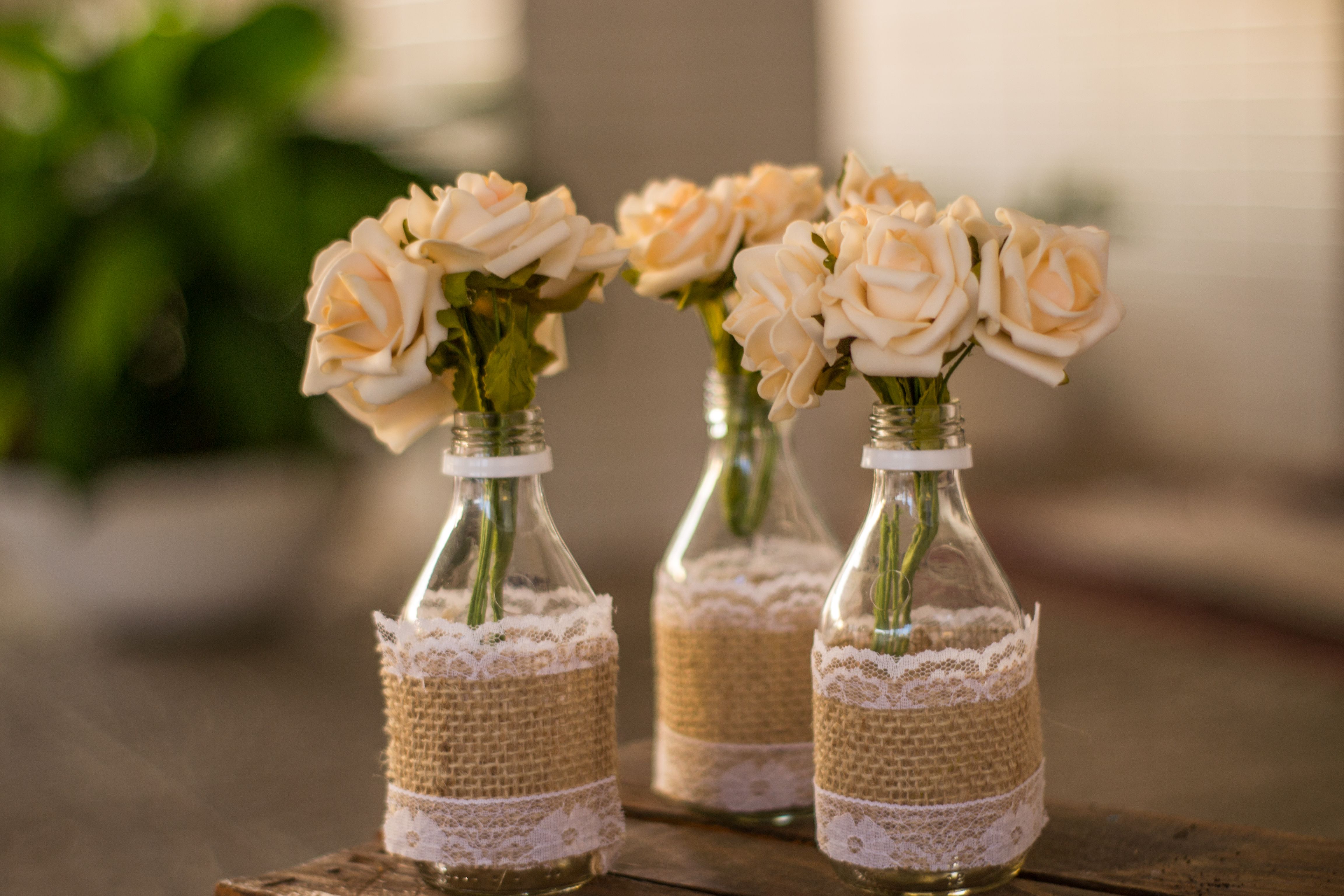 Cream roses arranged in handmade lace-covered vases as an inexpensive wedding centerpiece idea.