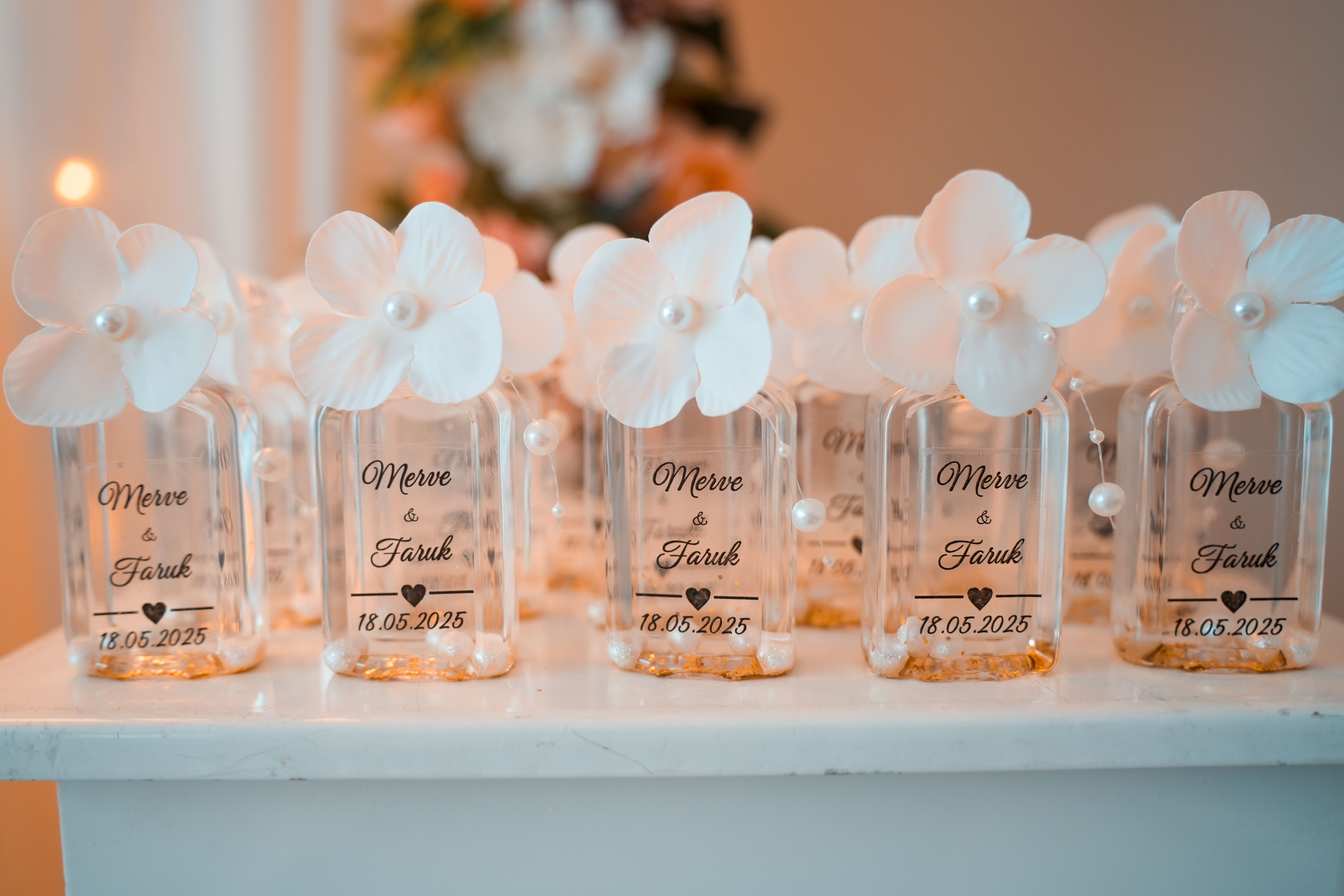 Wedding favor bottles with white flowers and personalized labels, a thoughtful budget-friendly guest favor.